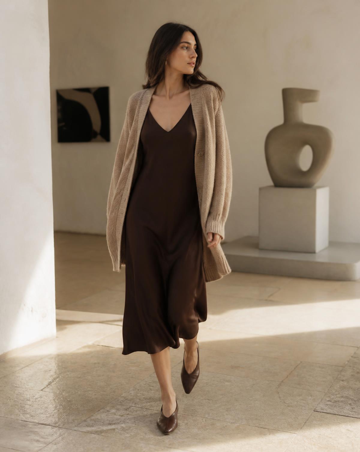 Woman in an espresso slip dress and beige cardigan in a minimal interior